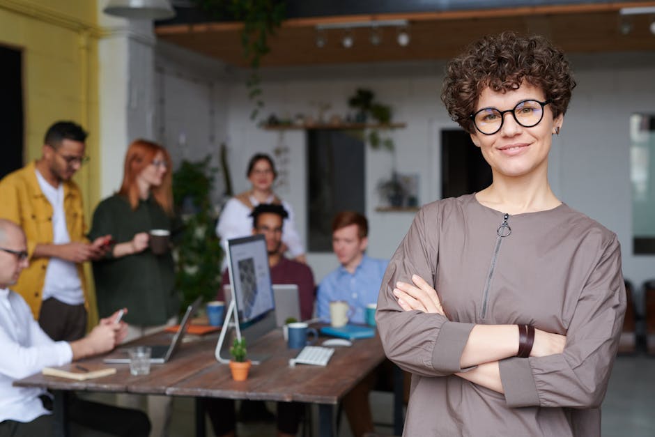Smiling businesswoman with curly hair stands confidently in a modern office space with colleagues